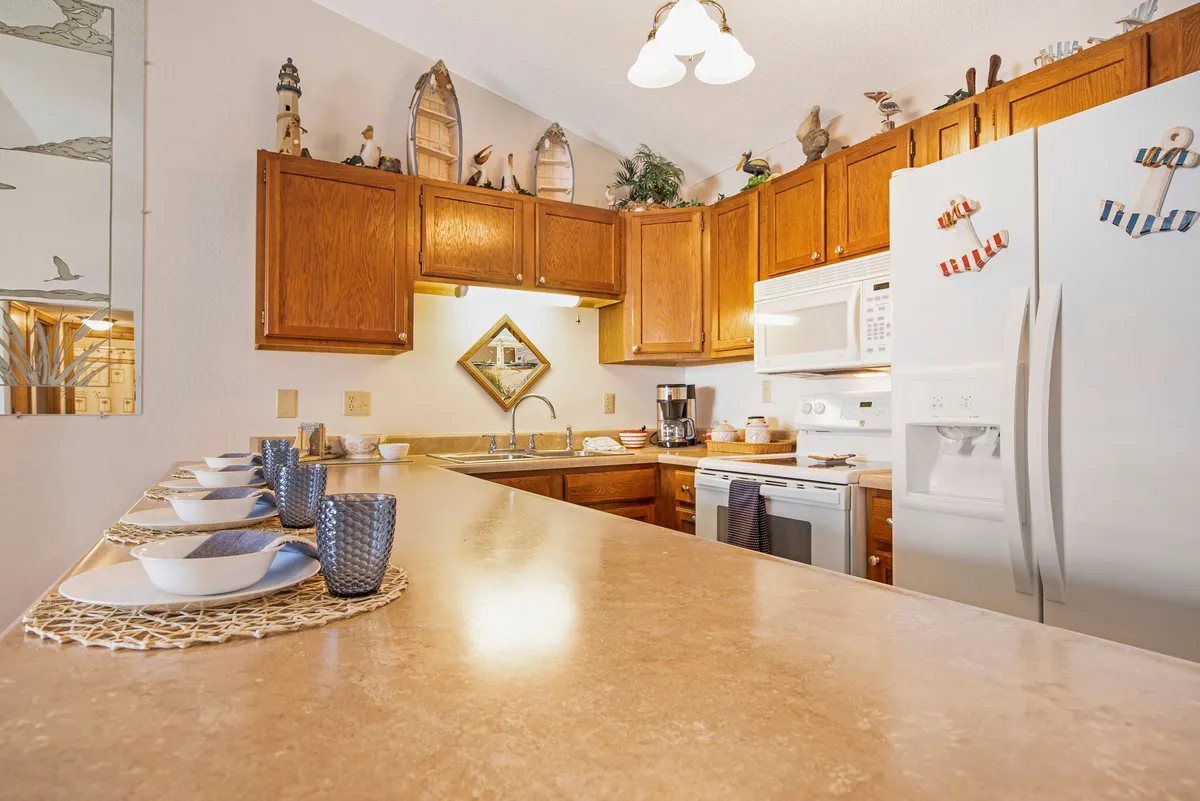 This image features a welcoming kitchen with a spacious counter, modern cabinets, appliances, and decorative items. The scene suggests a space designed for both cooking and socializing, with plenty of room for meal preparation and entertaining guests.