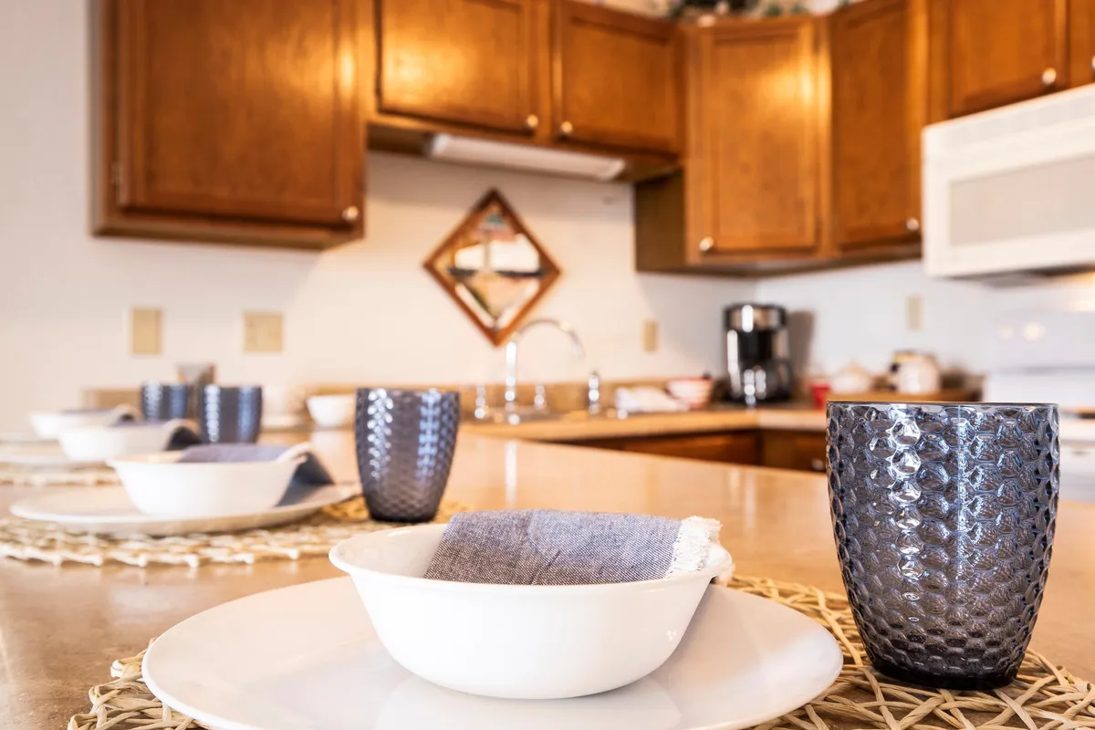 The image highlights a warm dining area with a beautifully set dining table, kitchen cabinetry in the background, and a decorative mirror. The setting feels inviting and is clearly designed to bring people together for shared meals.