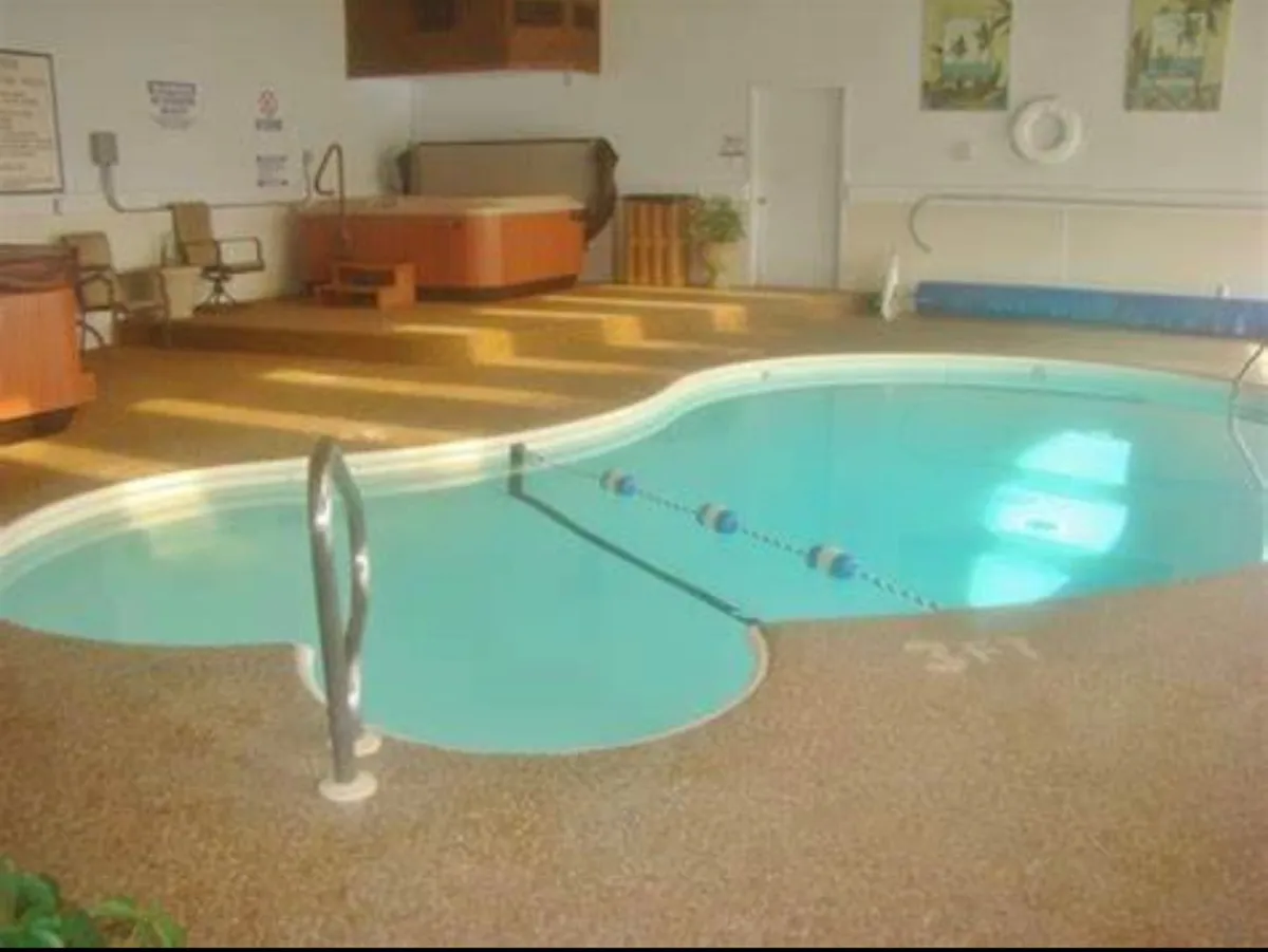 A bright interior scene showcasing both a swimming pool and a jacuzzi (hot tub) with lounge chairs lining the area. The sunlight streaming in adds a cheerful atmosphere, and the space is designed for relaxation and social gatherings.