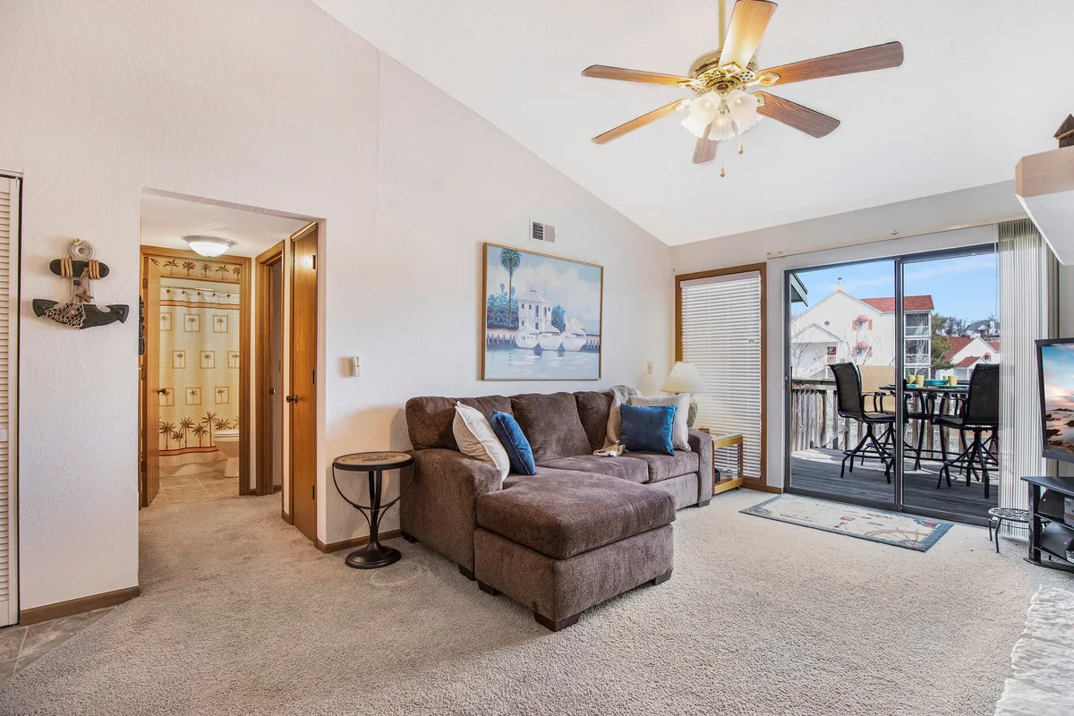 A cozy sectional sofa faces a large window and balcony, providing unobstructed views of the outdoors. Artwork enhances the tranquil atmosphere, and the space is ideal for relaxing, entertaining guests, or enjoying coffee while watching the sunset.
