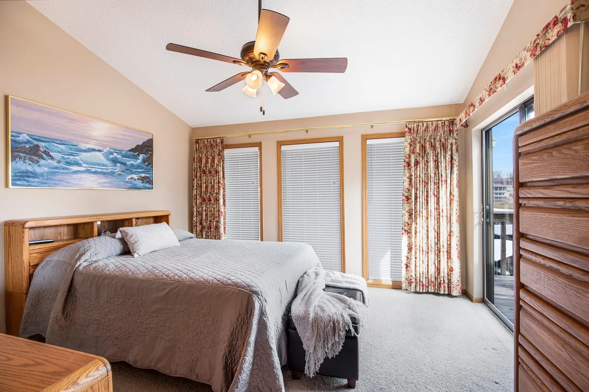 A peaceful bedroom featuring a large bed with crisp, soft bedding, tasteful window treatments that let in abundant natural light, and lakeside-inspired artwork on the walls. The space feels airy and tranquil, inviting rest and relaxation after a busy day.
