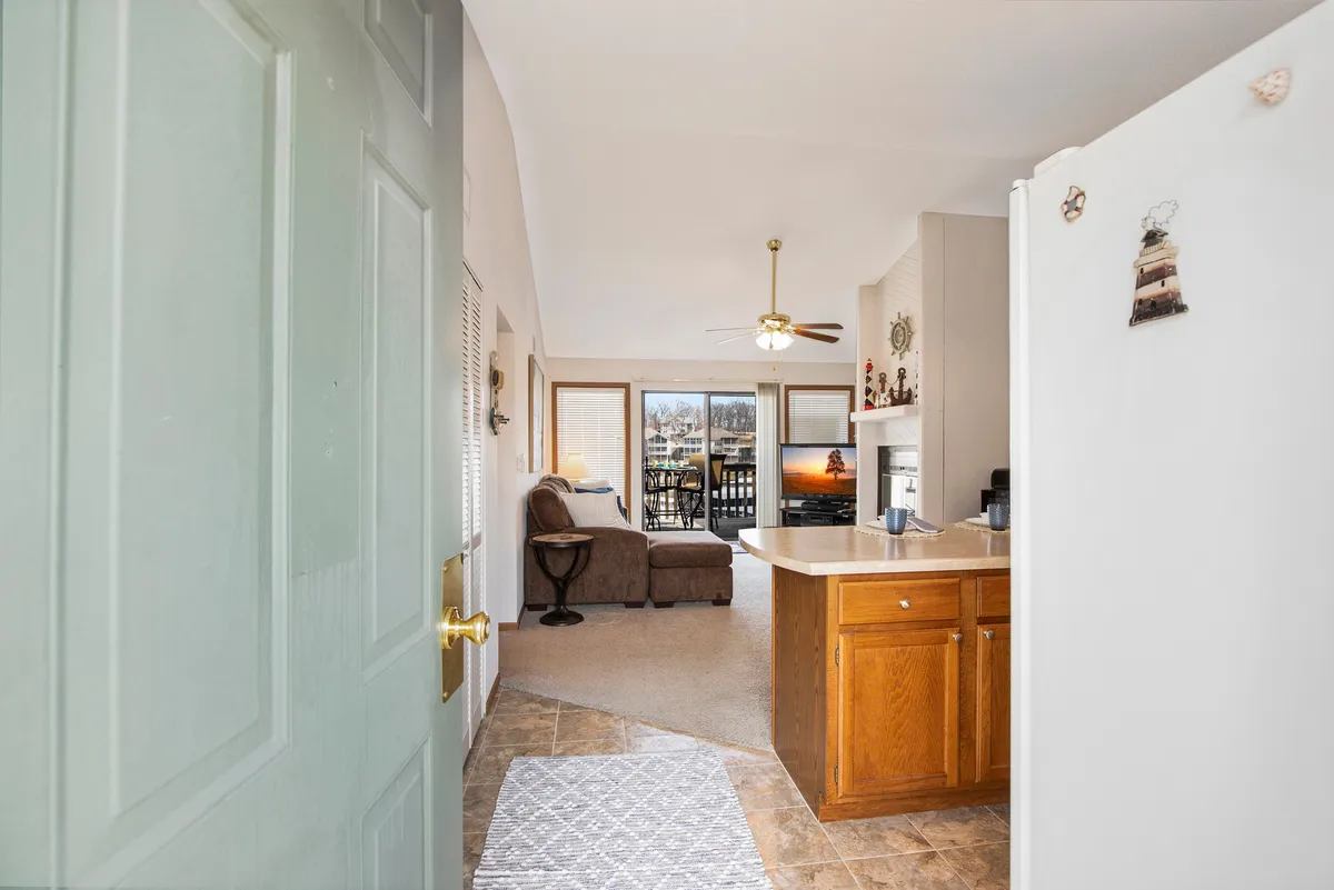 A sunlit living area with an open door leading to a balcony, offering views of the outdoors. The kitchen counter is set up for entertaining, and a plush sofa sits in the living space, creating an inviting atmosphere for socializing or relaxing. The balcony view hints at lakeside sunsets and the connection between interior comfort and the natural environment.